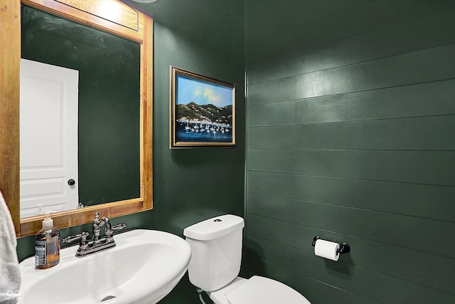 bathroom with toilet, wood walls, and a sink