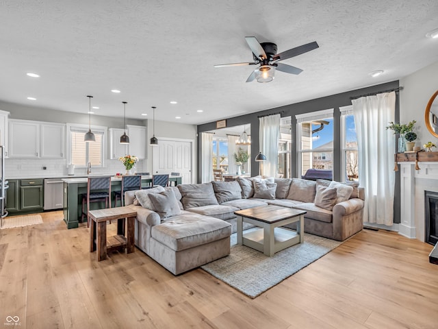 living area featuring a glass covered fireplace, a textured ceiling, light wood finished floors, and ceiling fan