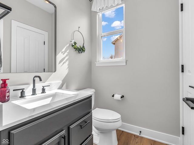 bathroom featuring baseboards, toilet, wood finished floors, and vanity