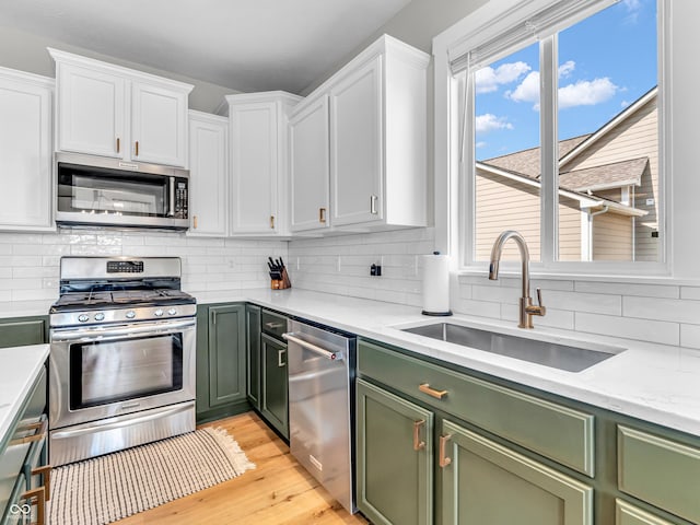 kitchen featuring a sink, decorative backsplash, stainless steel appliances, white cabinets, and green cabinets