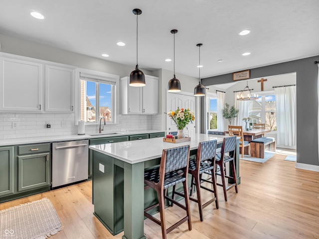 kitchen with green cabinets, light wood-style floors, stainless steel dishwasher, and a sink