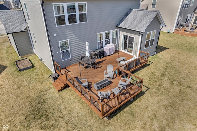 back of property featuring a wooden deck, a fire pit, a lawn, and roof with shingles