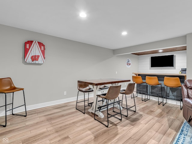 dining room featuring recessed lighting, baseboards, a bar, and light wood finished floors