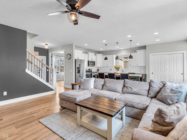 living room featuring stairway, light wood-style flooring, baseboards, and a healthy amount of sunlight