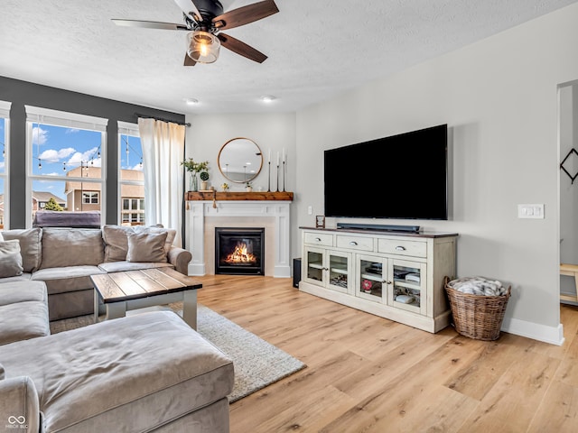 living room with a glass covered fireplace, wood finished floors, baseboards, and a textured ceiling