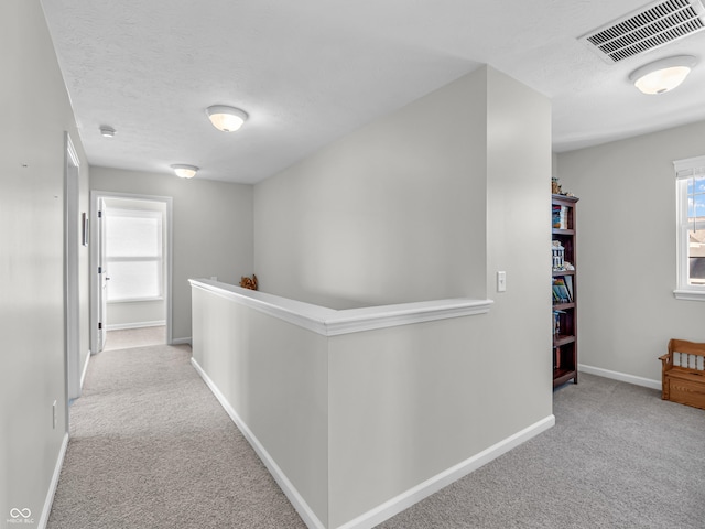 hall featuring visible vents, an upstairs landing, a textured ceiling, carpet floors, and baseboards