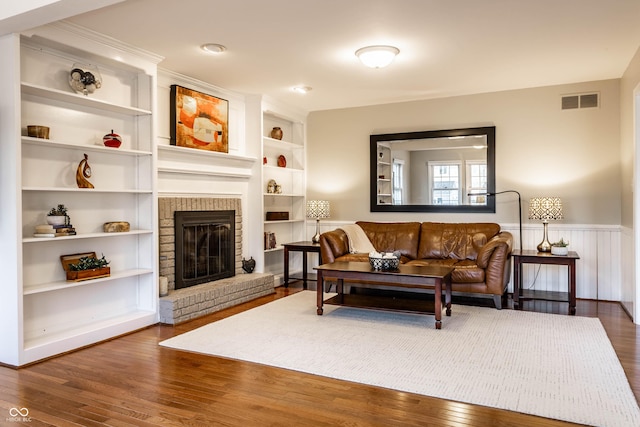 living room with a wainscoted wall, a brick fireplace, visible vents, and wood finished floors