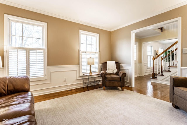 living area featuring visible vents, wood finished floors, wainscoting, crown molding, and stairs