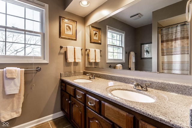 full bathroom featuring tile patterned flooring, double vanity, baseboards, and a sink