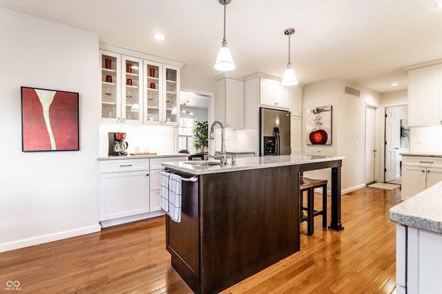 kitchen with light wood finished floors, visible vents, stainless steel fridge with ice dispenser, a center island with sink, and white cabinetry