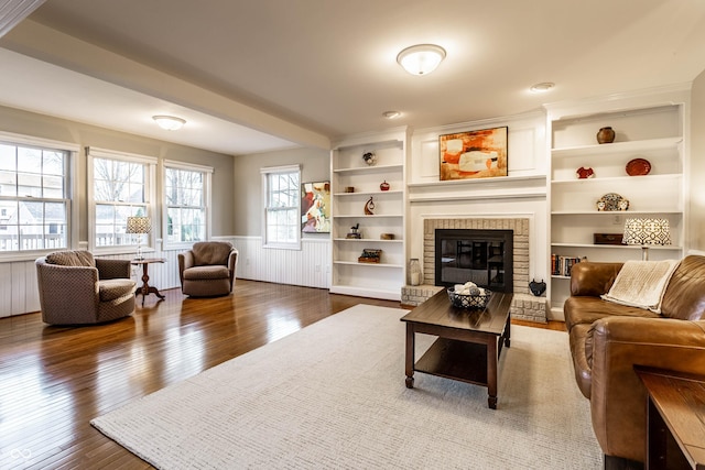 living area with hardwood / wood-style flooring, built in shelves, a fireplace, and a wainscoted wall