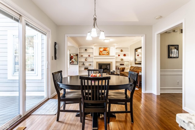 dining area featuring built in features, baseboards, wood-type flooring, and a fireplace