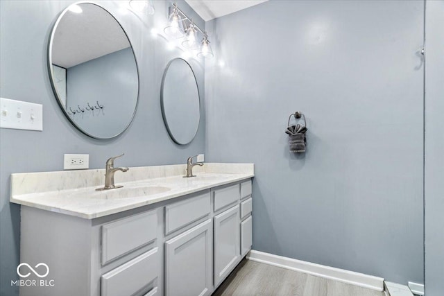 full bath featuring double vanity, wood finished floors, baseboards, and a sink