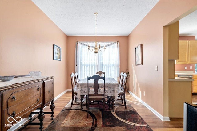 dining space featuring a notable chandelier, light wood-style floors, baseboards, and a textured ceiling