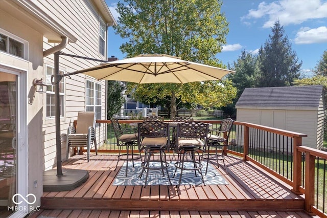 wooden terrace featuring an outbuilding, a shed, outdoor dining area, and fence