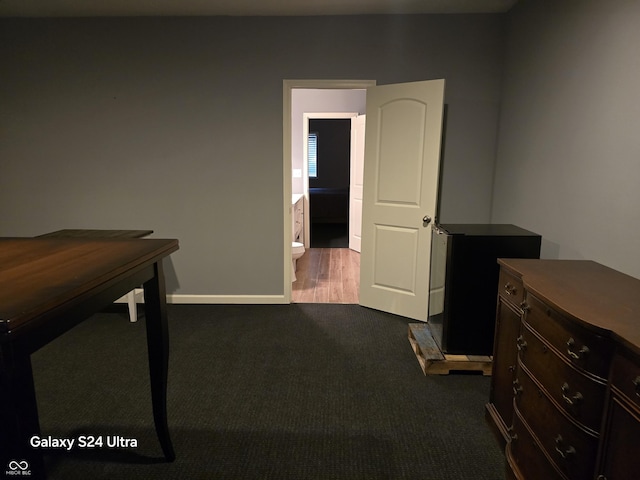 interior space with dark colored carpet, fridge, baseboards, and ensuite bathroom