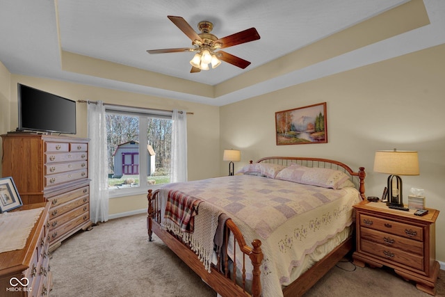 carpeted bedroom with baseboards, a raised ceiling, and ceiling fan