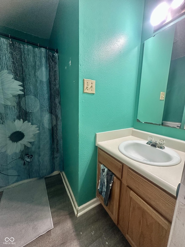 full bath featuring baseboards, a shower with curtain, wood finished floors, and vanity