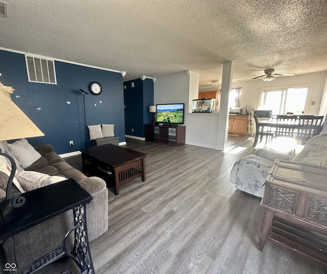 living room with a textured ceiling, wood finished floors, visible vents, and baseboards