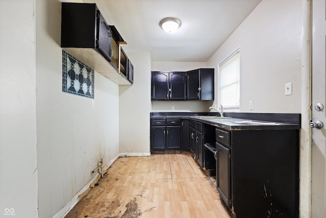 kitchen with light wood-style flooring, baseboards, dark cabinets, and a sink