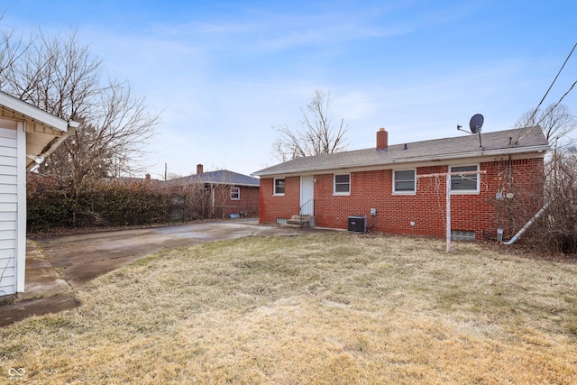 rear view of house featuring entry steps, central AC, a yard, brick siding, and a chimney