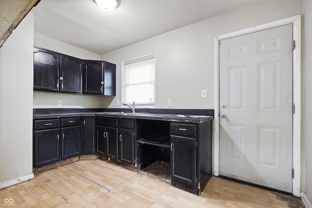 kitchen with dark cabinetry, dark countertops, light wood-type flooring, and a sink