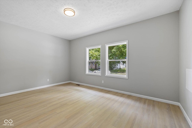 empty room featuring baseboards, light wood-type flooring, and a textured ceiling