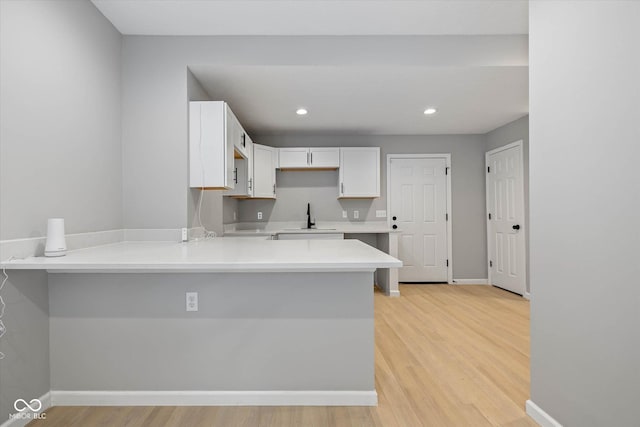 kitchen featuring a sink, a peninsula, light wood-style flooring, and white cabinetry