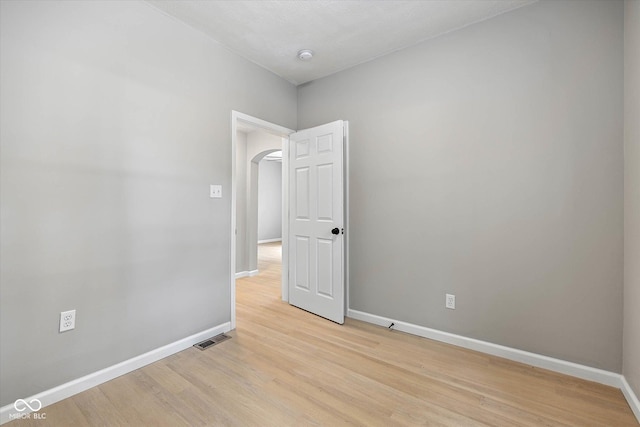 unfurnished room with light wood-type flooring, visible vents, arched walkways, and baseboards