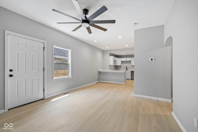 unfurnished living room with a ceiling fan, baseboards, recessed lighting, arched walkways, and light wood-style floors