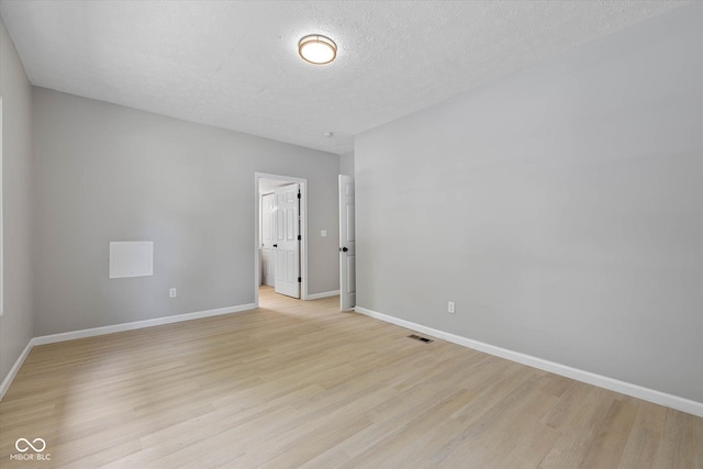 spare room featuring visible vents, light wood-style flooring, a textured ceiling, and baseboards