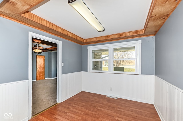 empty room featuring visible vents, wood finished floors, and wainscoting