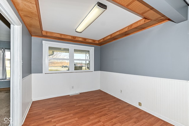 empty room with a wainscoted wall, a raised ceiling, visible vents, and wood finished floors