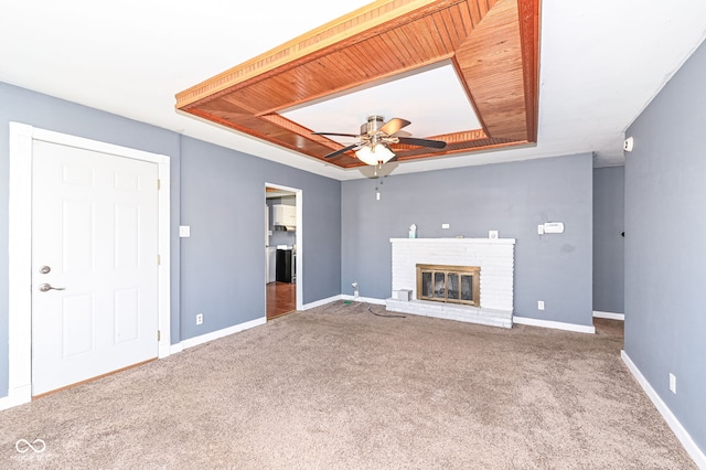 unfurnished living room with carpet, a tray ceiling, a fireplace, and baseboards