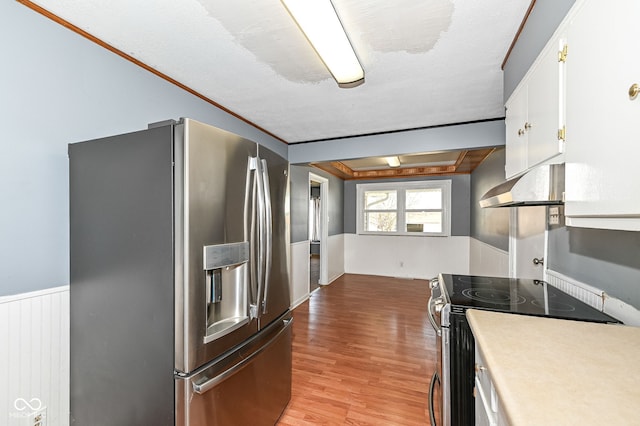 kitchen featuring a wainscoted wall, light wood-style flooring, range hood, white cabinetry, and appliances with stainless steel finishes