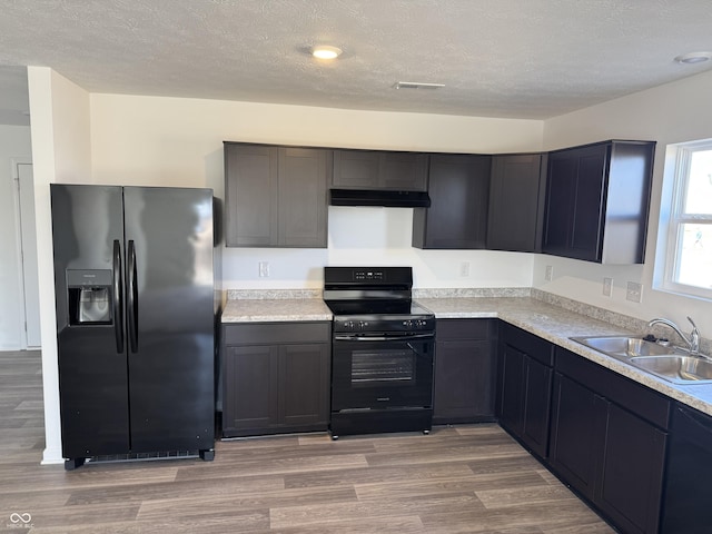 kitchen with light wood-type flooring, black appliances, a sink, under cabinet range hood, and light countertops