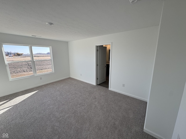 unfurnished room with a textured ceiling, baseboards, and dark colored carpet