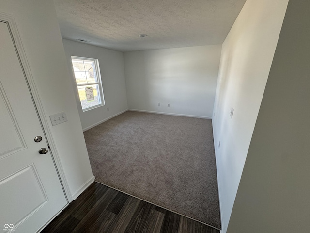 empty room featuring visible vents, baseboards, dark carpet, dark wood-style floors, and a textured ceiling