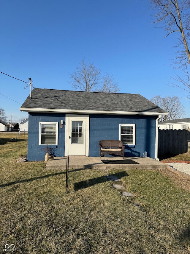 view of front of house featuring concrete block siding, a front lawn, fence, and a shingled roof