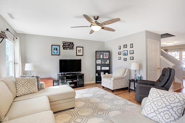 living room with a ceiling fan, visible vents, baseboards, stairs, and light wood-type flooring