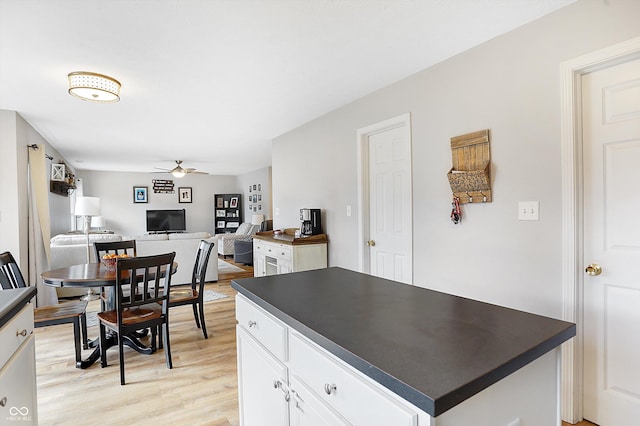 kitchen with light wood finished floors, a kitchen island, ceiling fan, white cabinetry, and dark countertops