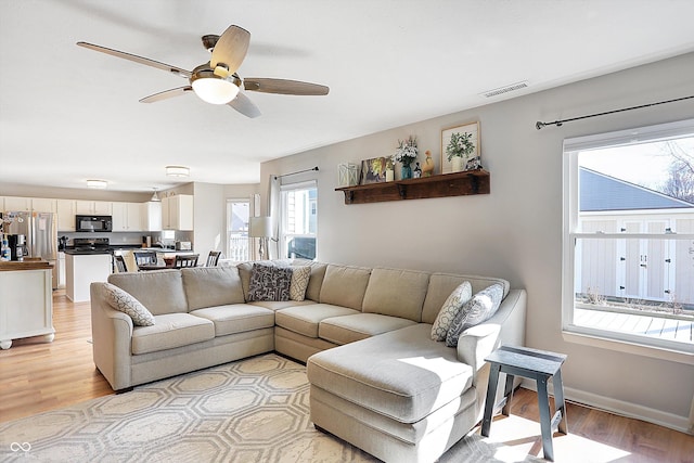 living area featuring visible vents, baseboards, light wood-style flooring, and a ceiling fan