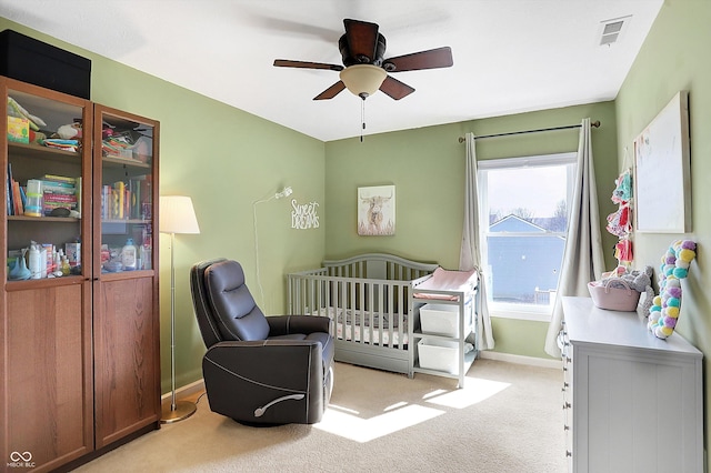 bedroom featuring visible vents, baseboards, ceiling fan, a nursery area, and light colored carpet