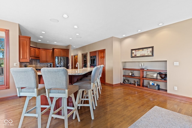 kitchen featuring black fridge with ice dispenser, light wood-style floors, wall oven, a kitchen breakfast bar, and brown cabinets
