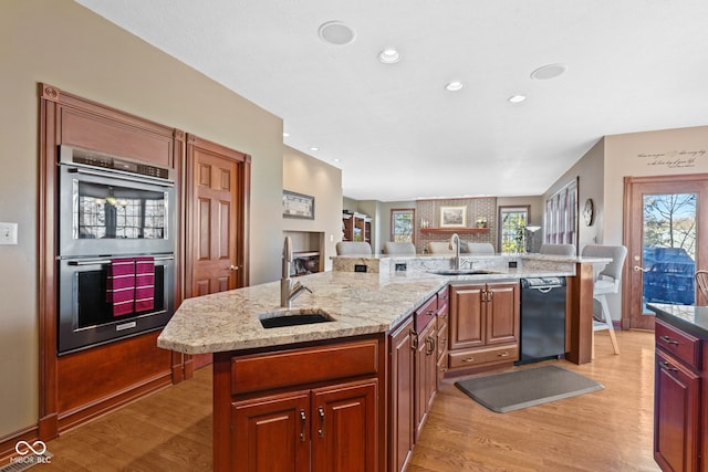 kitchen featuring a spacious island, light wood finished floors, black dishwasher, stainless steel double oven, and a sink