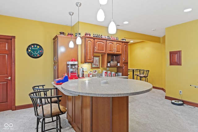 kitchen featuring a kitchen bar, decorative light fixtures, light colored carpet, and baseboards