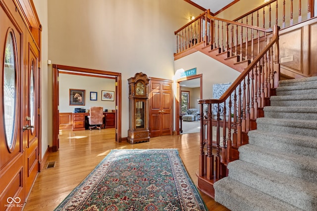 entryway with visible vents, stairway, light wood-style floors, and a towering ceiling