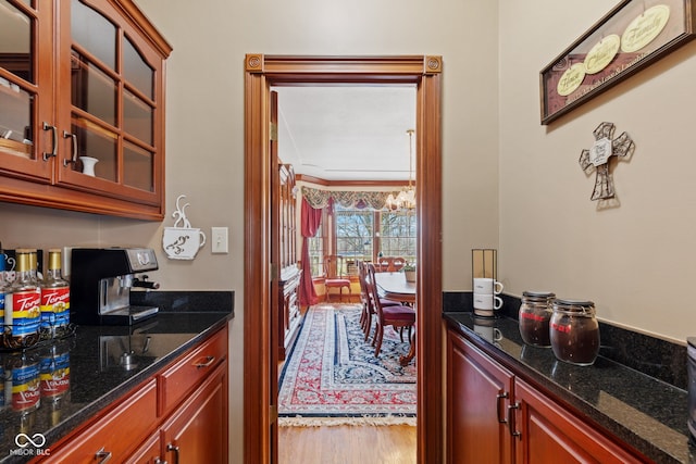 kitchen featuring a chandelier, dark stone countertops, glass insert cabinets, and wood finished floors