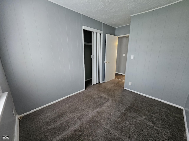 unfurnished bedroom featuring baseboards, dark carpet, and a textured ceiling