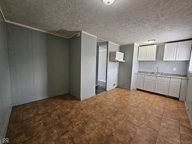 kitchen featuring a sink, a textured ceiling, white cabinetry, crown molding, and light countertops